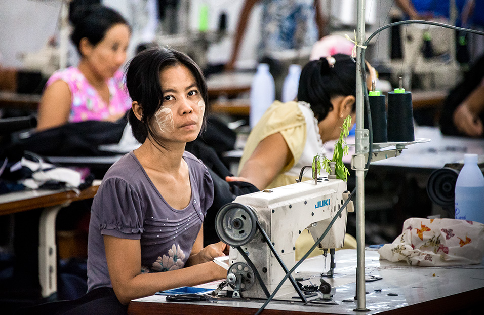 Myanmar migrant workers sew clothes in a factory in Thailand's western province of Mae Sot. Their working day runs from 7 am until 8 pm, including overtime, for which they earn less than 200 baht (6 dollars), well below the legal minimum wage of 305 baht. Their monthly income barely covers rent and food, leaving little opportunity for saving and reducing them to living day-to-day. This limited income security compounds other challenges that they face such as limited protections in housing, labour contracts and healthcare. Photo: UN Women/Piyavit Thongsa-Ard