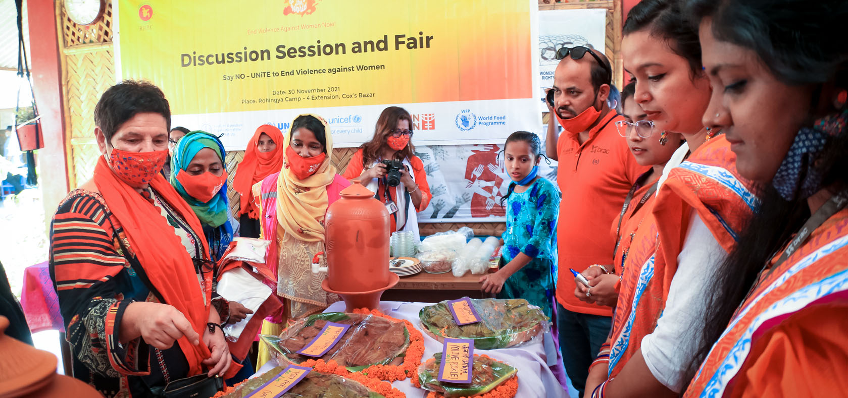 Flora Macula, left, UN Women Sub-office Head in Cox’s Bazar, Bangladesh, buys traditional Bengali food at a fair UN Women helped organize in Rohingya Camp-4 Extension in Cox’s Bazar on 30 November 2021. The fair was part of events during the United Nations 16 Days of Activism against Gender-based Violence. Photo: UN Women/Shataw Nur
