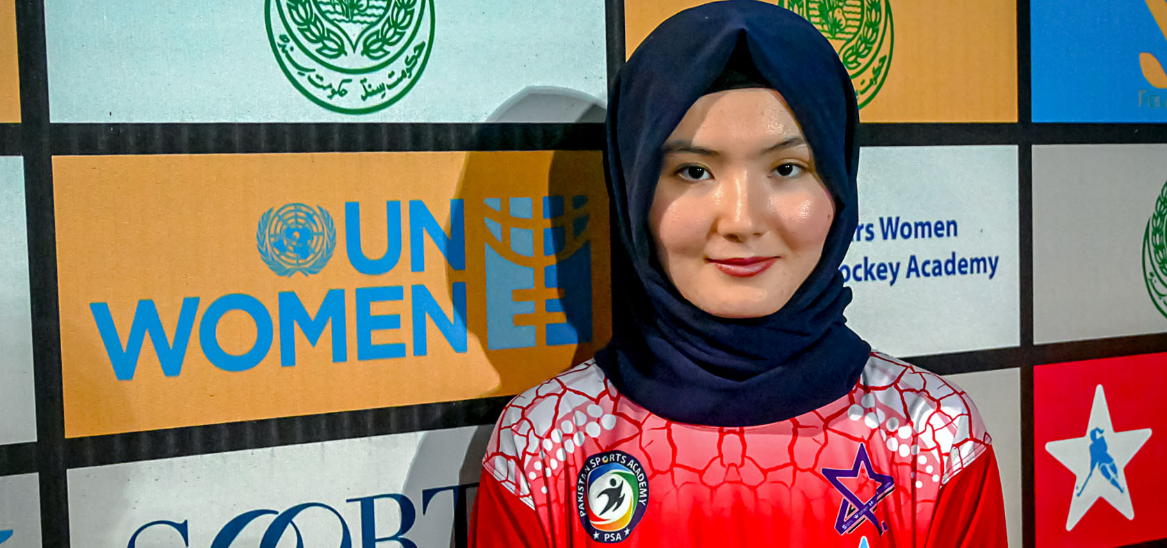 A woman stands in front of the UN Women banner with her sports attire
