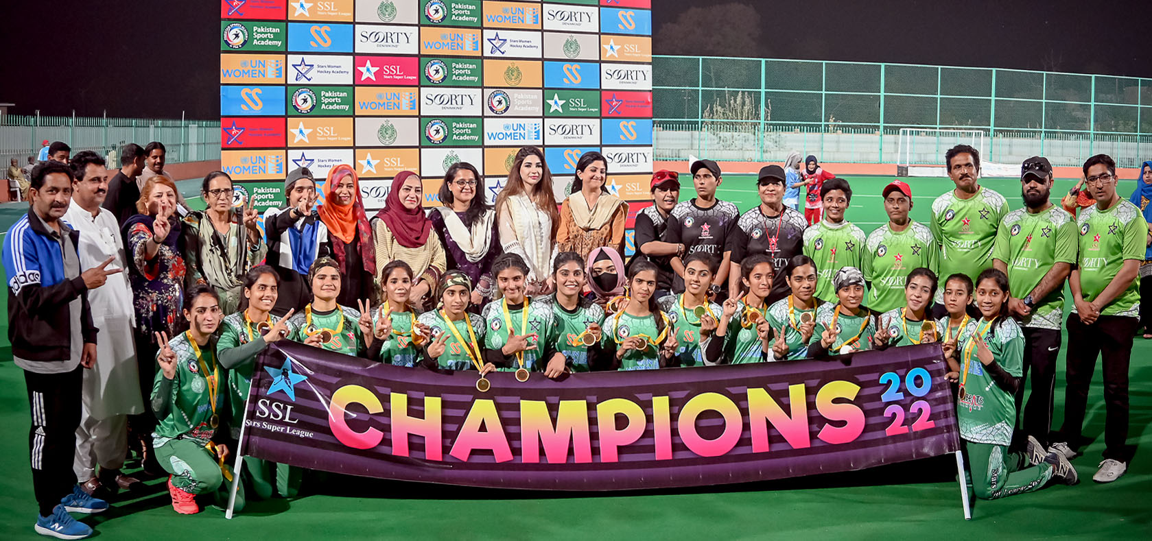 A group of female footballers taking photo in the field with their coaches and male staff