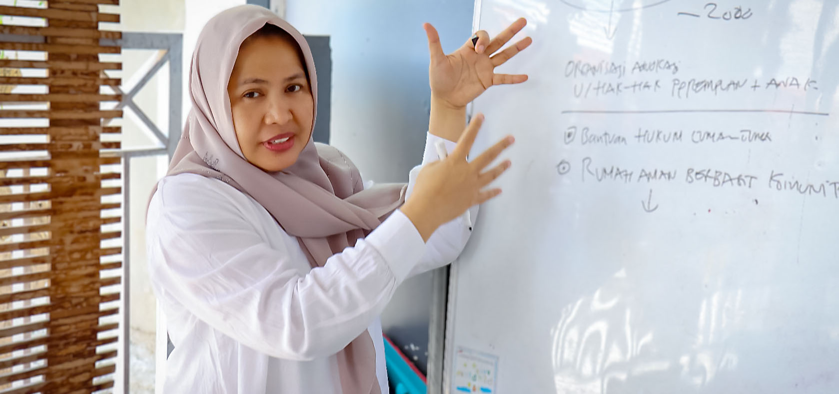 Dewi Rana wearing hijab is explaining something as shown in the whiteboard in from of her.