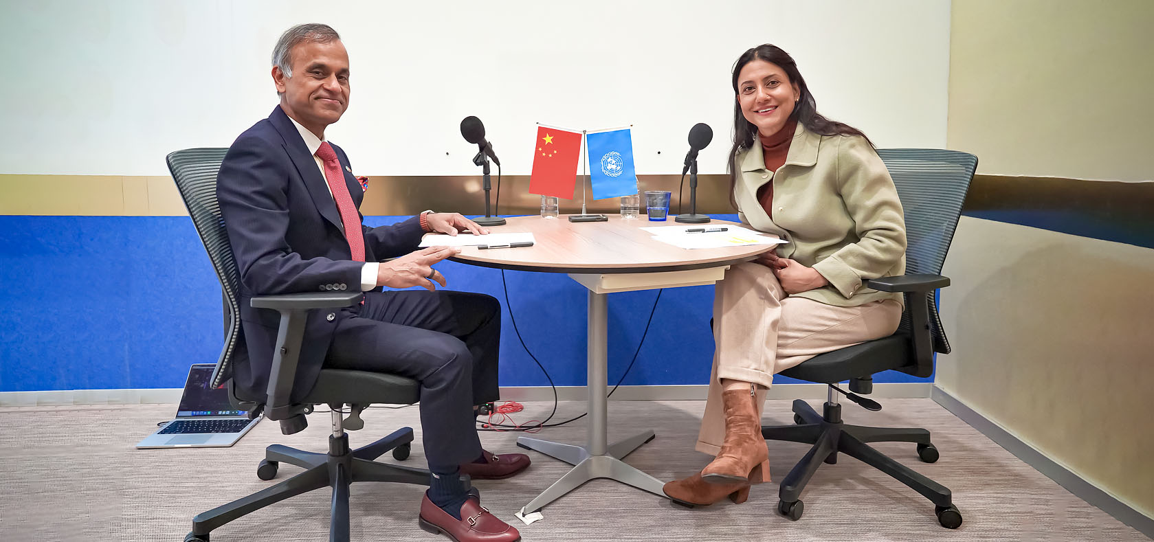 [from left] Siddharth Chatterjee and Smriti Aryal sit on a their chairs around the table with Microphones, ready for doing podcast. They are facing the camera. Photo taken for UN Women by Zhao Wenting