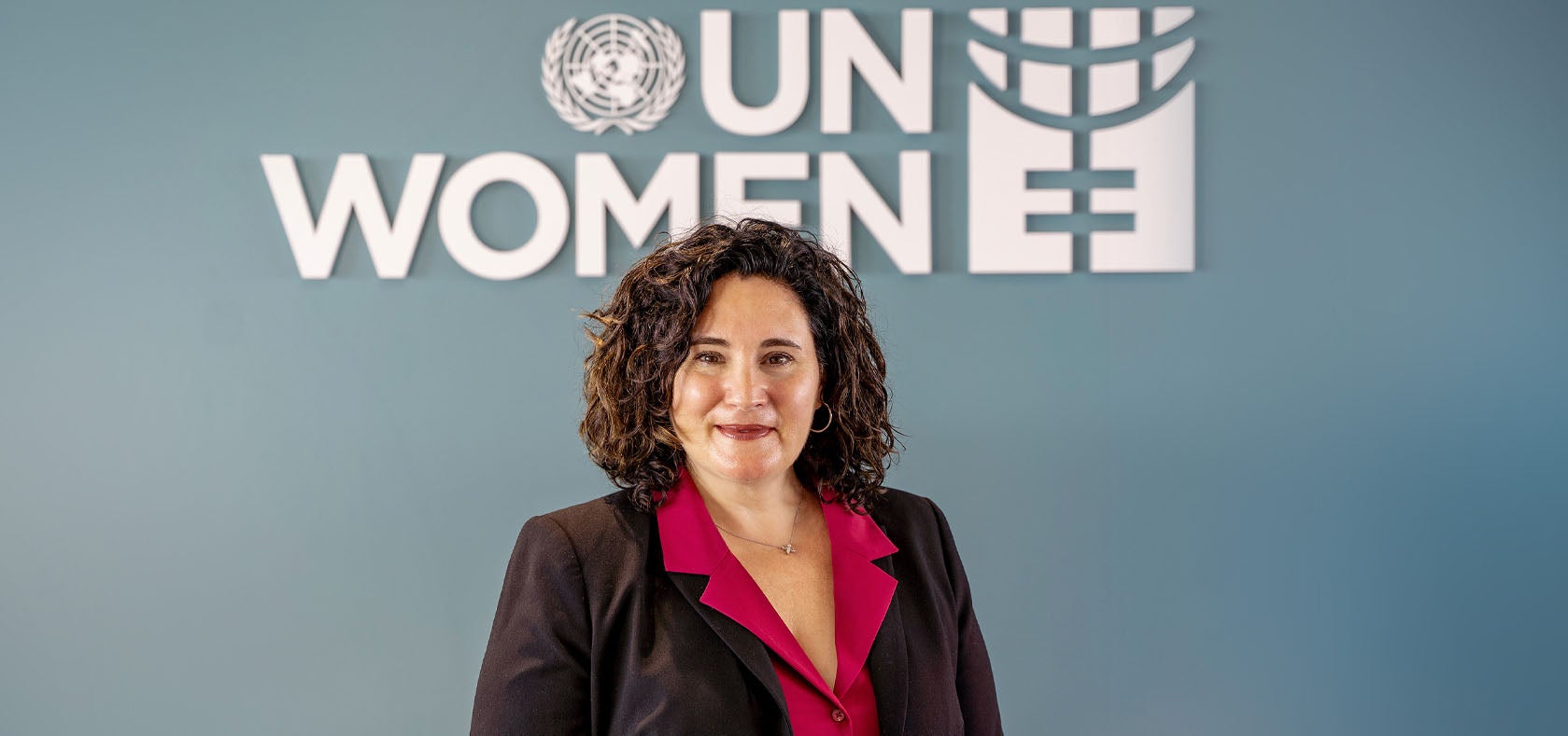 Christine Arab, Regional Director of UN Women Asia-Pacific, standing in front of a grey-blue wall with white UN Women logo in the middle, above her head. Photo: UN Women/Pairach Homtong