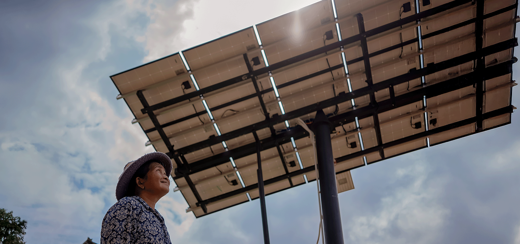 An old Cambodia woman standing happyly underneath the solar cell installed on the top of a pole.