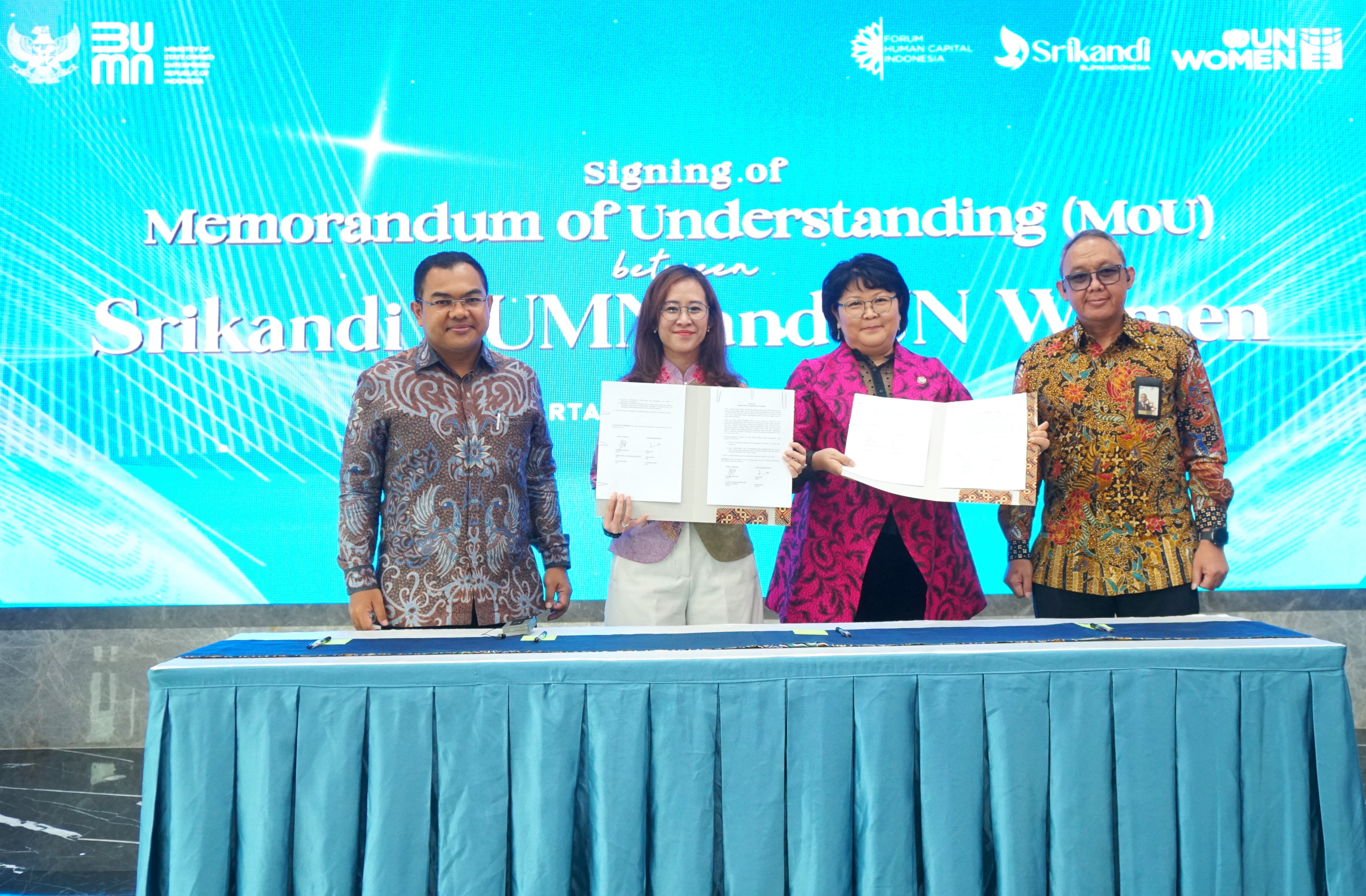 Four people standing behind a desk. Two women are at the center, holding a signed Memorandum of Understanding