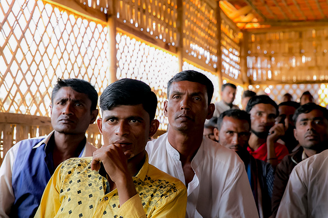 Rohingya men look on as UN Women Executive Director, Phumzile Mlambo-Ngcuka meets with CIC's in charge of camps, Shamimul Huq Pavel, Muhammed Talut, and ASM Obaidullah in Balukhali Rohingya Refugee camp February 1, 2018 in Chittagong division, Bangladesh. They listen to the Executive Director's engaging the room, "Keep your daughters at school to learn their life skills. Women are able to contribute to the society and the community when they reach their full potentials." Photo: UN Women/Allison Joyce