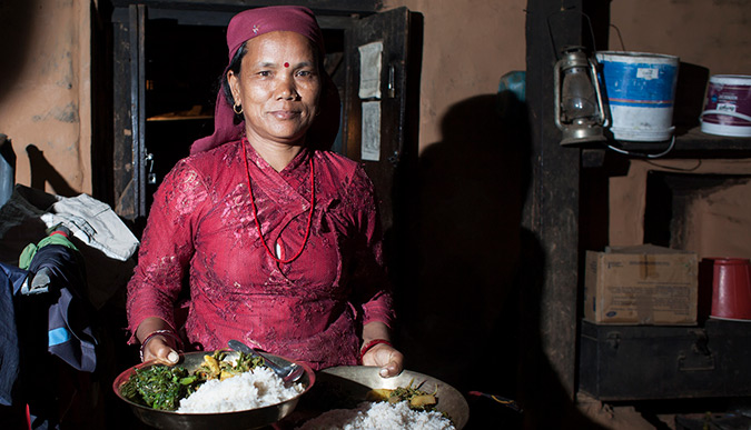 Puspa Kumari Gurung, running a home stay in Lwang Gaon, Nepal, serves dinner to the guests- a traditional Nepali thali that includes a chicken curry, spinach, lentils, potatoes, rice and chutney.   Photo: Vidura Jang Bahadur