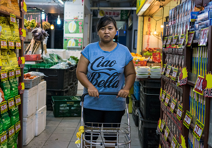 Nurachayatun Siti, a 35-year-old Indonesian domestic helper from Surabaya Java, does the family shopping early Saturday morning, 25 November 2017, in Sembawang Hills Estates, Singapore. This is Nur's second job as a domestic worker in Singapore. The first when she was 19, was a painful and demoralizing situation where her employers had her sleep on the floor for two years, with little food, no time off, and S$20 per month, the rest of her wages were either withheld or taken by the agency that placed her. The end came when her employer accused her of theft. She gladly left. This time she has returned on her own terms earning well about the average $550. On her one day off, Nur is learning how to sew, meets with friends, and attends labour law discussions to better protect herself.  Photo: UN Women/Staton Winter