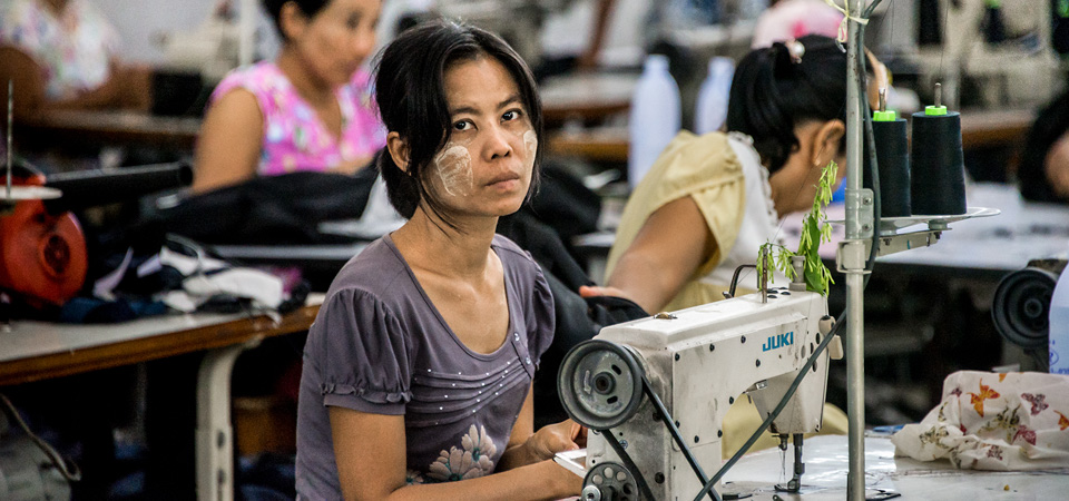 Myanmar migrant workers sew clothes in a factory in Thailand's western province of Mae Sot. Their working day runs from 7 am until 8 pm, including overtime, for which they earn less than 200 baht (6 dollars), well below the legal minimum wage of 305 baht. Their monthly income barely covers rent and food, leaving little opportunity for saving and reducing them to living day-to-day. This limited income security compounds other challenges that they face such as limited protections in housing, labour contracts and healthcare.  Photo: UN Women/Piyavit Thongsa-Ard