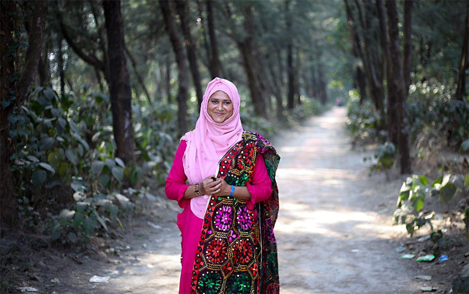 Photo of Umme Kulsum standing on a small road surounding by big trees. Photo: UN Women