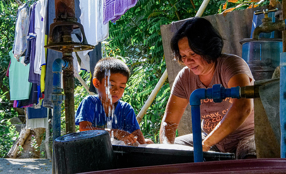Dory Olinoy is joined by her son Rainier while doing the laundry. Both her two sons have to stay inside the compound as the running community quarantine is forbidding kids to get out of the streets to play amidst the coronavirus crisis. Photo: UN Women/Louie Pacardo