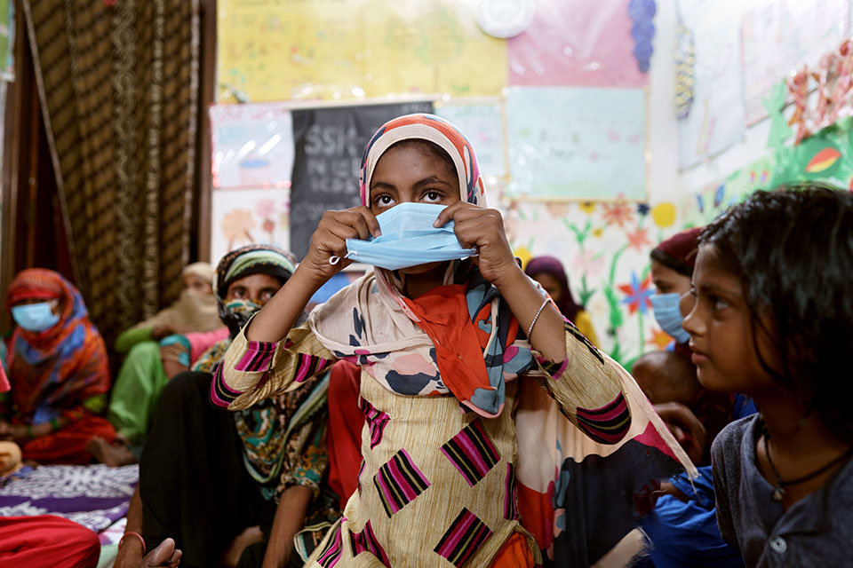 Women and children from the community assembled at a Saheli Samanvay Kendra (SSK) centre in Batla House, Delhi. In this photo, 12-year-old Nazra is learning to put on a mask and listening to Rehana Chaton explain the benefits of handwashing and masking as part of COVID-19 prevention. Photo: UN Women/Ruhani Kaur