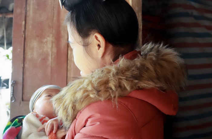 The ethnic minority woman living with HIV in Dien Bien City, Viet Nam, holds her grandson in front of her house on 10 December 2021. Photo: UN Women/Thao Hoang